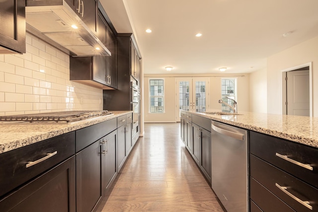 kitchen featuring backsplash, appliances with stainless steel finishes, wood finished floors, a sink, and ventilation hood
