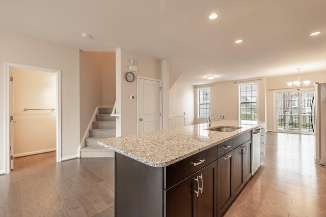 kitchen with an inviting chandelier, wood finished floors, a center island with sink, a sink, and appliances with stainless steel finishes
