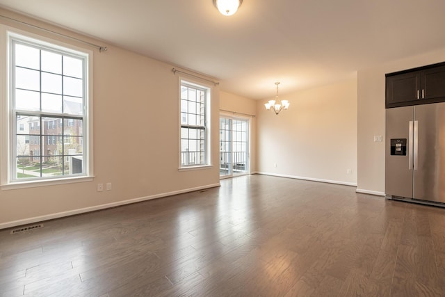 unfurnished living room with an inviting chandelier, dark wood-style flooring, visible vents, and a healthy amount of sunlight
