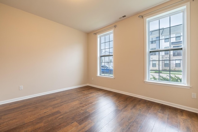 empty room featuring baseboards, visible vents, and dark wood-style floors