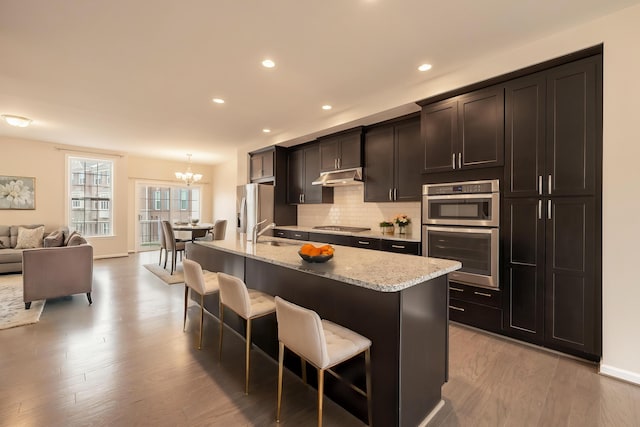 kitchen featuring appliances with stainless steel finishes, a sink, a chandelier, a kitchen bar, and under cabinet range hood