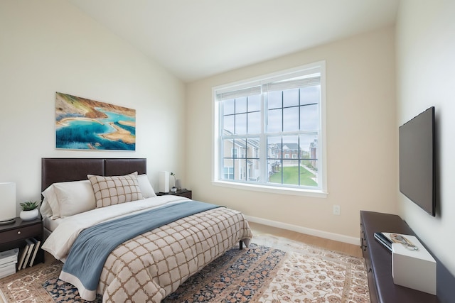 bedroom featuring baseboards, multiple windows, vaulted ceiling, and light wood-type flooring