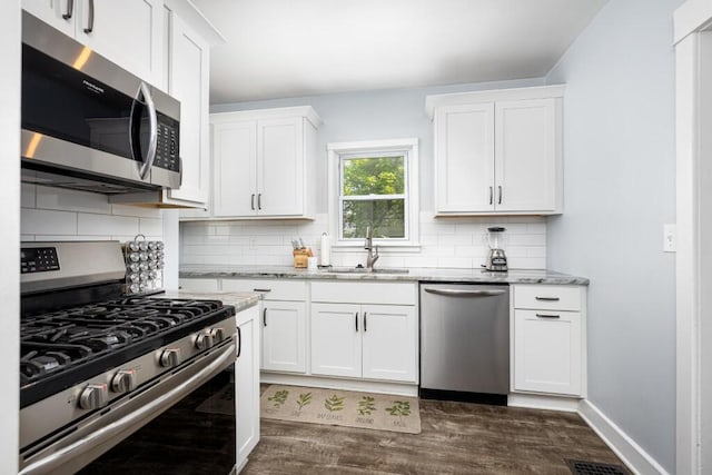 kitchen featuring light stone counters, a sink, stainless steel appliances, tasteful backsplash, and dark wood-style floors