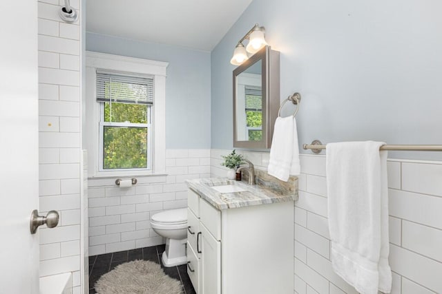 full bath with vanity, toilet, tile walls, tile patterned floors, and a wainscoted wall
