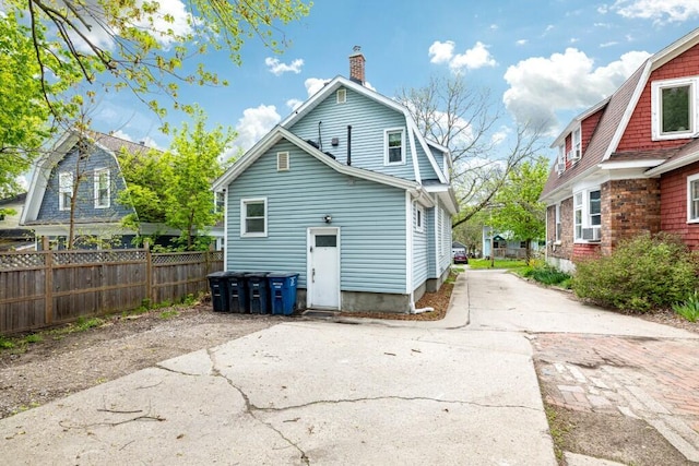 rear view of property with a gambrel roof, fence, driveway, and a chimney