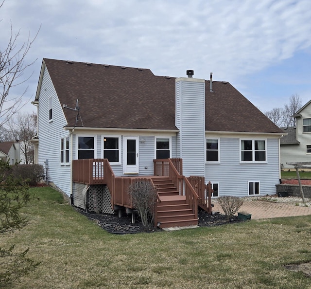 back of house featuring roof with shingles, a wooden deck, a chimney, and a yard