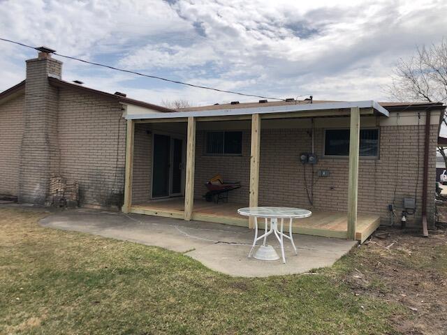 back of house featuring a yard, brick siding, a chimney, and a patio area