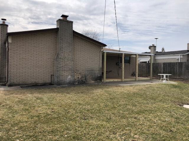 back of property featuring fence, a patio, a chimney, brick siding, and a lawn