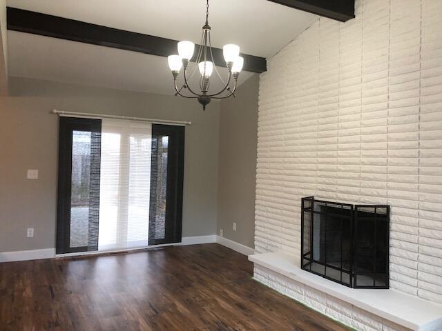 unfurnished living room with baseboards, an inviting chandelier, wood finished floors, and a fireplace