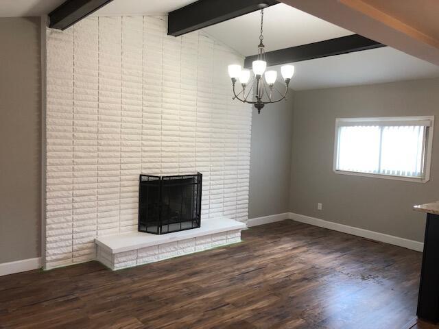 unfurnished living room featuring a brick fireplace, a chandelier, baseboards, vaulted ceiling with beams, and wood finished floors