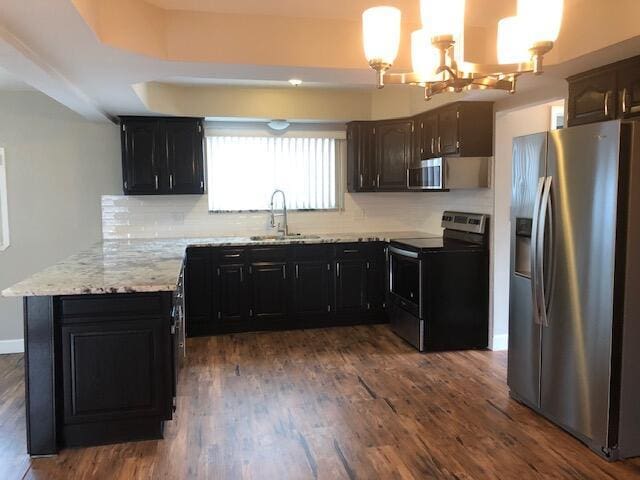 kitchen featuring backsplash, appliances with stainless steel finishes, a sink, a peninsula, and an inviting chandelier