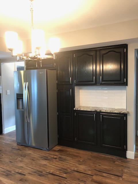 kitchen with light stone counters, stainless steel fridge, a chandelier, dark wood-type flooring, and backsplash