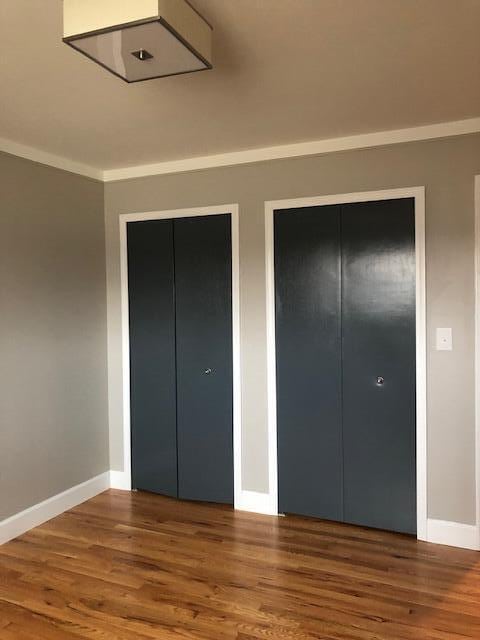 unfurnished bedroom with baseboards, multiple closets, and wood finished floors