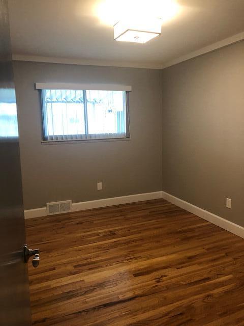 empty room with dark wood finished floors, ornamental molding, a healthy amount of sunlight, and visible vents