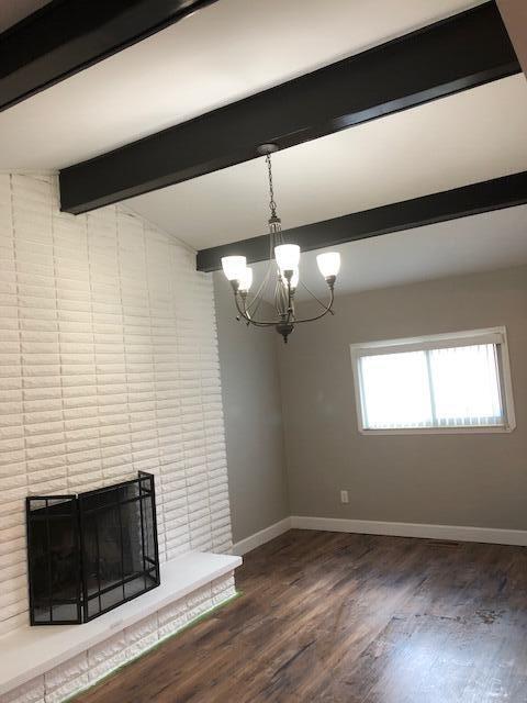 unfurnished dining area featuring a brick fireplace, baseboards, a chandelier, and wood finished floors