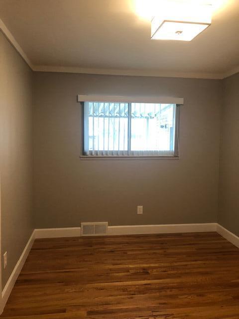 spare room featuring crown molding, wood finished floors, and a healthy amount of sunlight