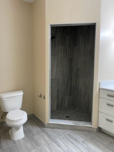 bathroom featuring vanity, toilet, baseboards, and a stall shower