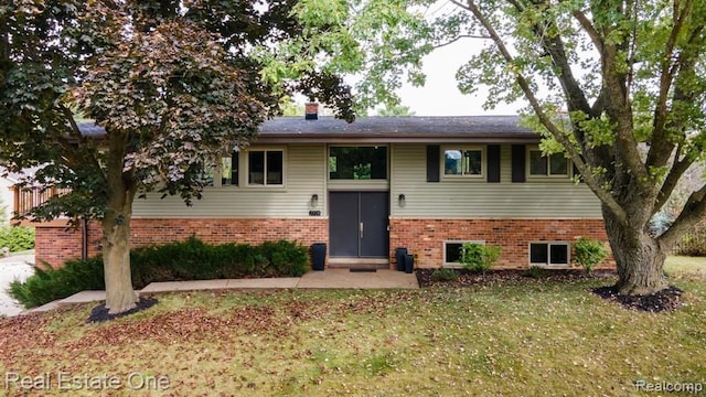 split foyer home featuring a chimney, a front lawn, and brick siding