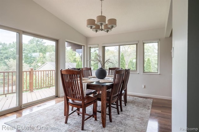 dining area featuring a notable chandelier, visible vents, baseboards, wood finished floors, and vaulted ceiling