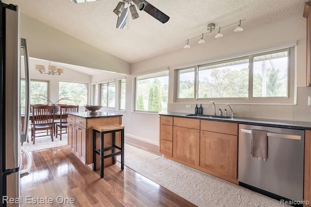 kitchen featuring wood finished floors, dark countertops, a textured ceiling, a sink, and appliances with stainless steel finishes