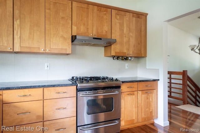 kitchen featuring under cabinet range hood, dark wood finished floors, stainless steel gas range oven, and dark stone countertops