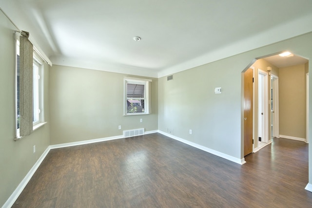 empty room featuring arched walkways, dark wood-style flooring, and baseboards