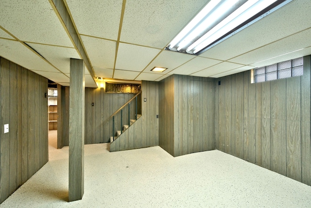 below grade area featuring stairs, wood walls, and a drop ceiling