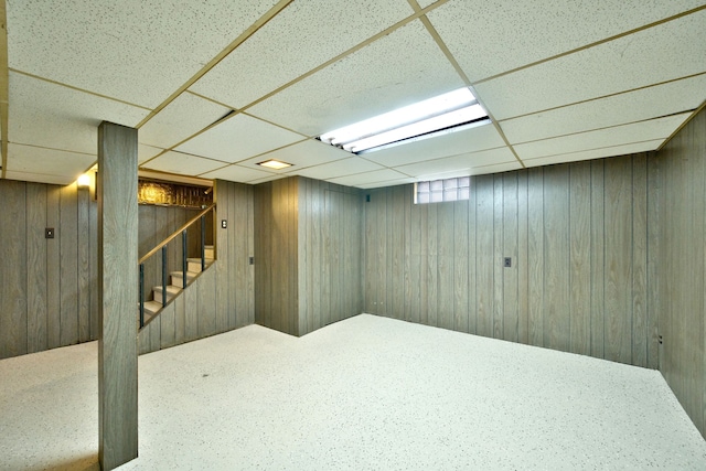 below grade area with stairs, a drop ceiling, wooden walls, and carpet flooring
