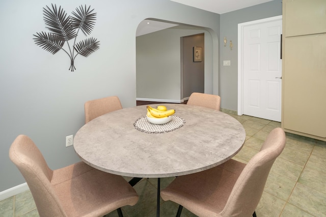 dining area featuring baseboards, arched walkways, and light tile patterned flooring