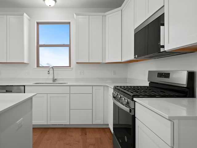 kitchen featuring light wood-type flooring, light countertops, white cabinetry, a sink, and stainless steel appliances