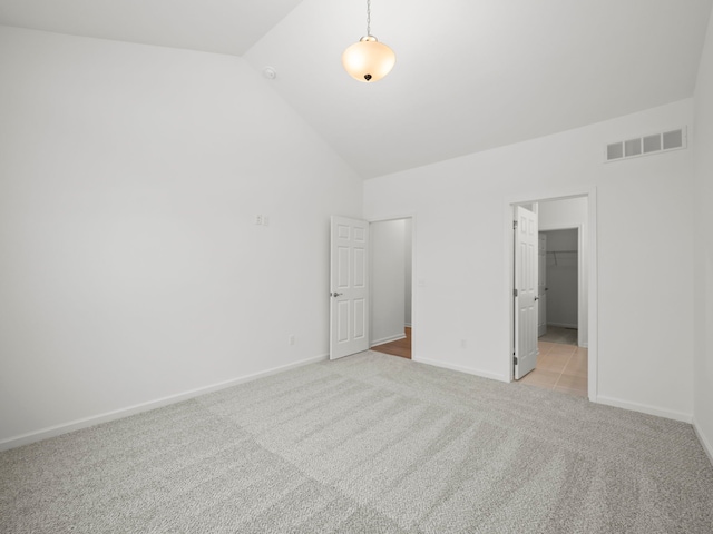 unfurnished bedroom featuring light colored carpet, baseboards, a spacious closet, lofted ceiling, and visible vents