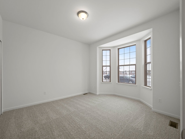 empty room featuring baseboards, visible vents, and light carpet