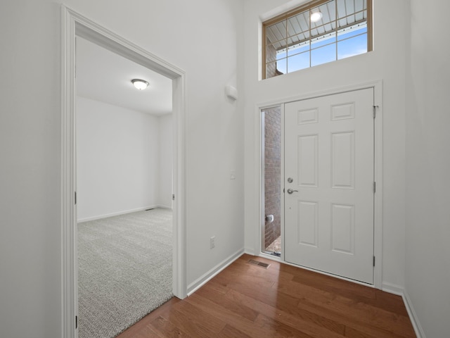 foyer entrance with baseboards, wood finished floors, and visible vents