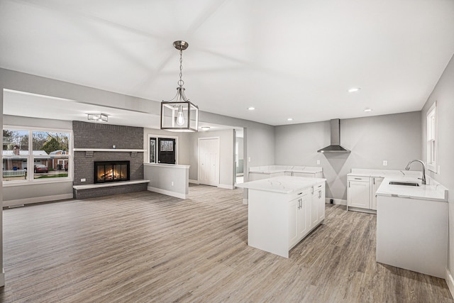 785 Maple Dr, Columbiaville, MI 48421 - kitchen with light wood-style flooring, a sink, a brick fireplace, white cabinets, and wall chimney range hood