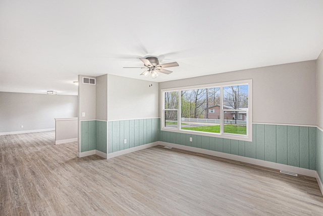 785 Maple Dr, Columbiaville, MI 48421 - empty room with ceiling fan, visible vents, a wainscoted wall, and wood finished floors