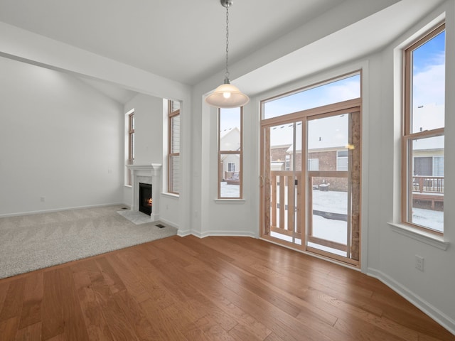 unfurnished living room featuring plenty of natural light, a fireplace with flush hearth, baseboards, and wood finished floors