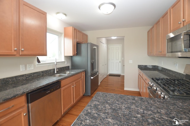 kitchen with dark stone countertops, appliances with stainless steel finishes, a sink, and wood finished floors