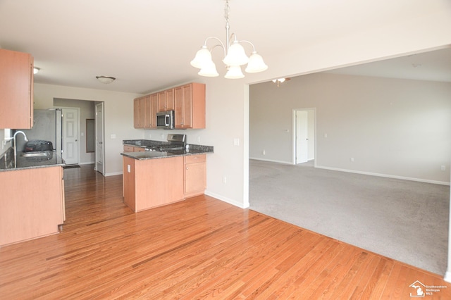 kitchen with an inviting chandelier, a sink, dark stone counters, stainless steel appliances, and open floor plan