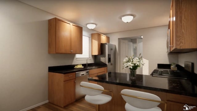 kitchen featuring brown cabinetry, a peninsula, a kitchen bar, a sink, and stainless steel appliances