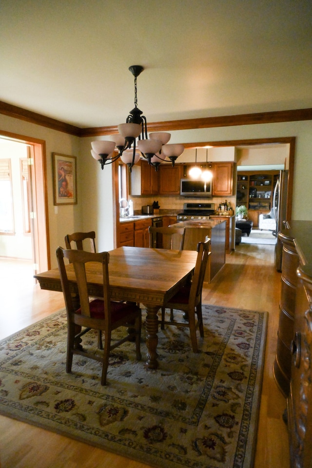 dining room with light wood-type flooring, a chandelier, and ornamental molding