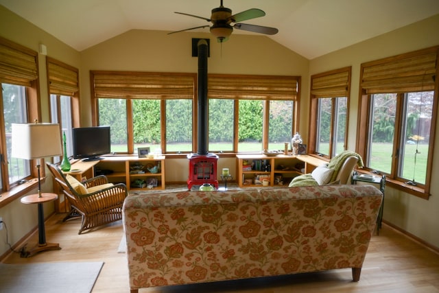 living area with vaulted ceiling, a wood stove, a ceiling fan, and light wood-style floors