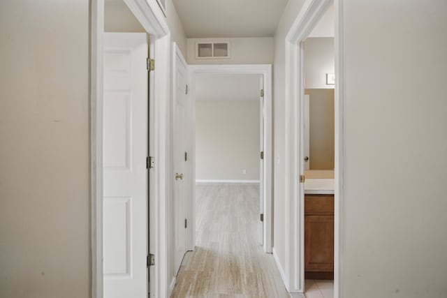 hallway featuring baseboards, visible vents, and light wood-style floors