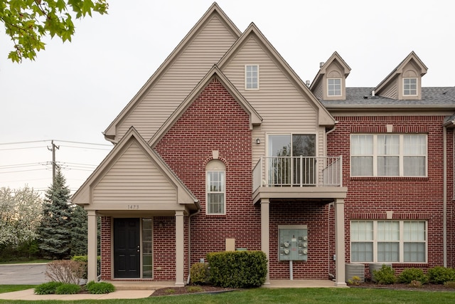 view of front facade with brick siding, roof with shingles, and a balcony