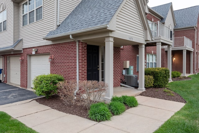 view of home's exterior with roof with shingles, brick siding, driveway, a garage, and cooling unit
