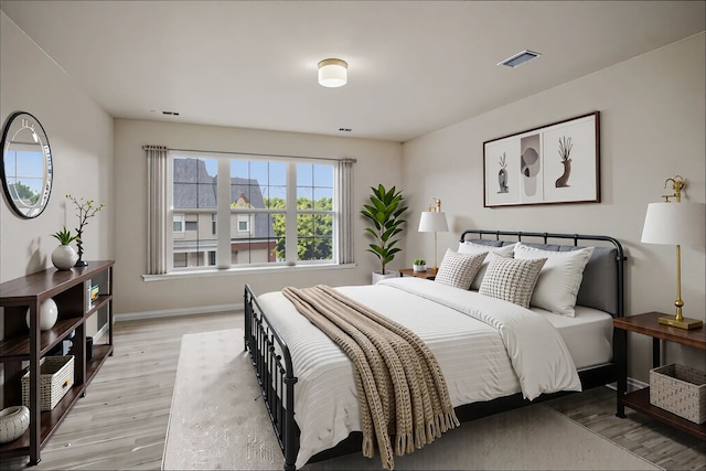 bedroom with baseboards, light wood finished floors, and visible vents