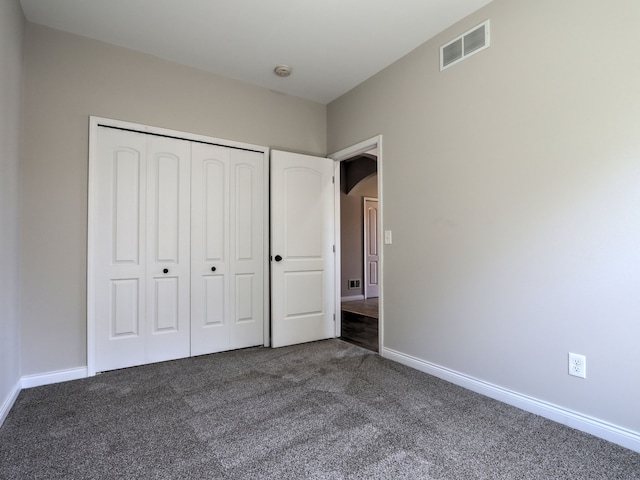 unfurnished bedroom with baseboards, a closet, dark carpet, and visible vents
