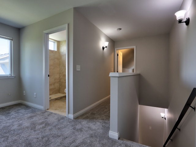 corridor featuring carpet floors, baseboards, and an upstairs landing