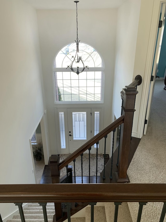 carpeted foyer featuring stairs, an inviting chandelier, and a towering ceiling