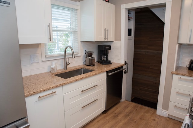 kitchen featuring freestanding refrigerator, dishwashing machine, backsplash, and a sink