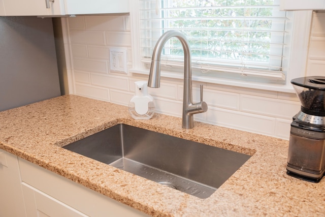 details featuring a sink, white cabinetry, decorative backsplash, and light stone counters